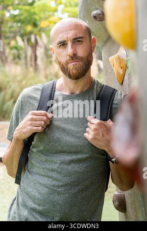 Portrait of a bearded man with shaved head standing next to an outdoor climbing wall. Stock Photo