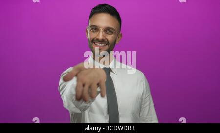 Young hispanic man in a white shirt and tie smiling warmly against a vivid pink background, reaching forward with an inviting gesture, exuding a profe Stock Photo