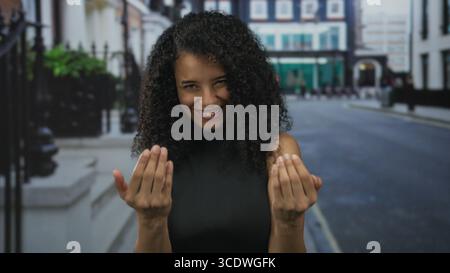 Young hispanic woman beckons with both hands forward on quiet city street; invitation greeting friendly. Stock Photo