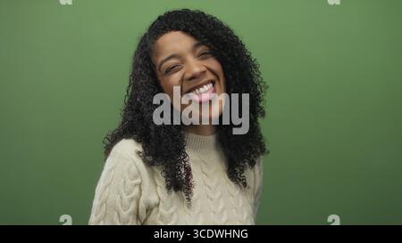 African american woman in cream cable knit sweater sticks her tongue out and squints eyes in studio; playfulness. Stock Photo