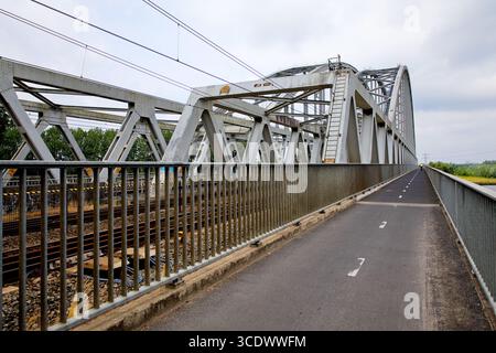Steel truss railway bridge with separated cycle path over river in the Netherlands, converging lines and overhead wires shaping a transport scene. Stock Photo