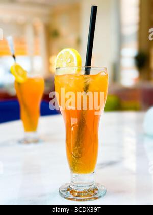A tall glass of iced tea with lemon slices and a black straw on a marble table in a bright hotel bar setting in Dubai, UAE Stock Photo