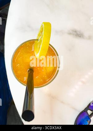 A tall glass of iced tea with lemon slices and a black straw on a marble table in a bright hotel bar setting in Dubai, UAE Stock Photo
