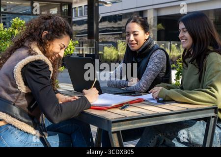 University students collaborating on a project outdoors: utilizing technology and teamwork for academic success Stock Photo