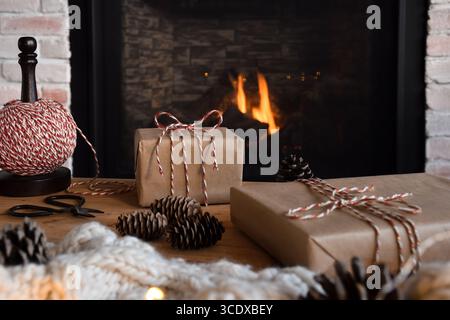 Wrapped Christmas gifts in simple brown paper tied with red and white string in front of a fireplace at home Stock Photo