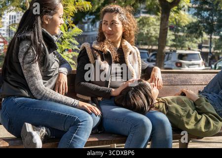 Three young women enjoying a relaxing afternoon, chatting and bonding on a park bench Stock Photo