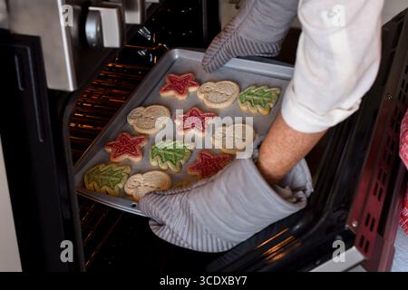 Woman is taking out freshly baked Christmas cookies out of the oven Stock Photo