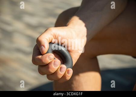 Man strengthens his grip using hand black rubber expander. He is seen holding expander with firm grip, suggesting focused exercise. Close up. Stock Photo