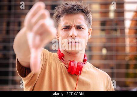 Man with red headphones showing thumbs down gesture with serious expression Stock Photo