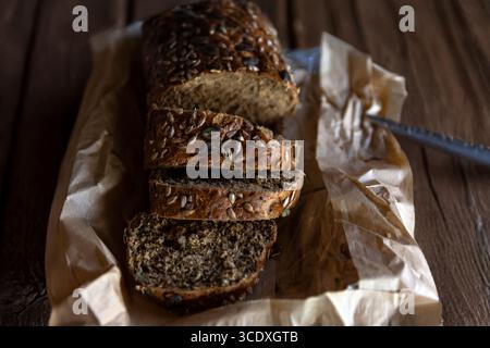 Sliced multigrain bread loaf with mixed seeds on brown paper, placed on a rustic wooden table, perfect for bakery or food concepts. Stock Photo