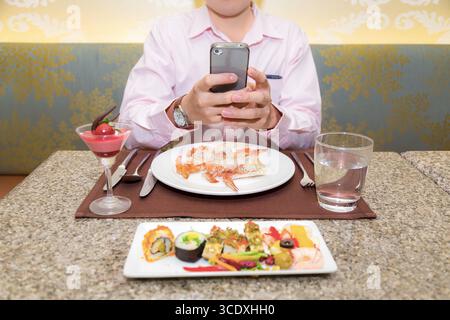 Young businessman text messaging on a smart phone during meal in a restaurant. Stock Photo