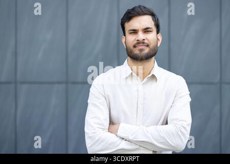 Young man dressed formally, showcasing confidence while posing against a contemporary blue-gray background. Ideal for themes of professionalism, confidence, and success. Stock Photo