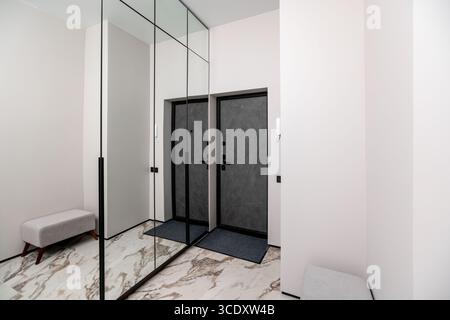 A hallway with a mirror on the wall and a couch in the middle. The hallway is white and the mirror is large Stock Photo