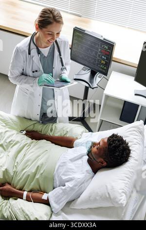 Vertical high angle view of cheerful young adult doctor greeting young Black man after waking up from coma Stock Photo
