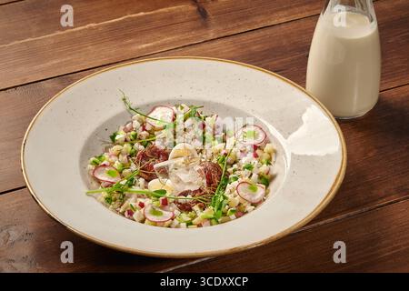 Okroshka decorated with pea sprouts being served with kefir on wooden table Stock Photo