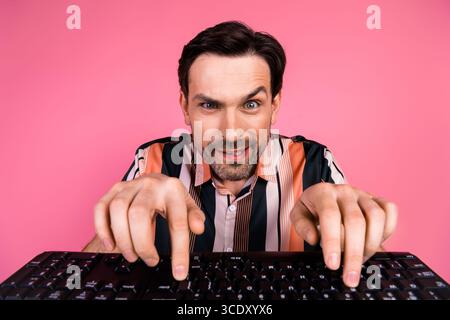 Young man energetically typing on keyboard with playful expression in pink background showcasing modern lifestyle Stock Photo