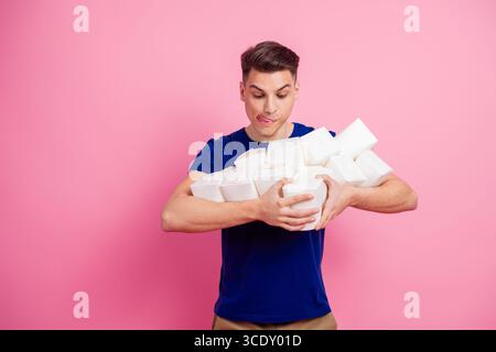 Young man holding multiple food boxes in a playful gesture against a pink background, showcasing casual style and humor Stock Photo