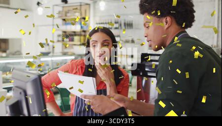 Reviewing printed report cafe staff wearing aprons at counter with espresso maker and gold confetti. Cafe, camaraderie, celebration, warm ambiance, te Stock Photo