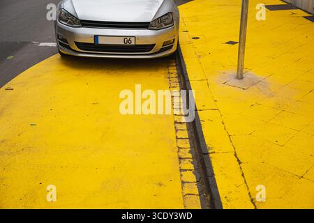 Silver car parked on a vivid yellow-painted street corner Stock Photo