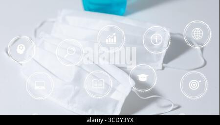 Displaying two surgical masks and blue sanitizer on white desk, overlaying digital interface icons. Health, hygiene, safety, technology, medical, well Stock Photo