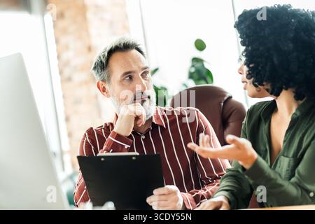 Two business professionals discussing a project in an office environment during a focused brainstorming session Stock Photo
