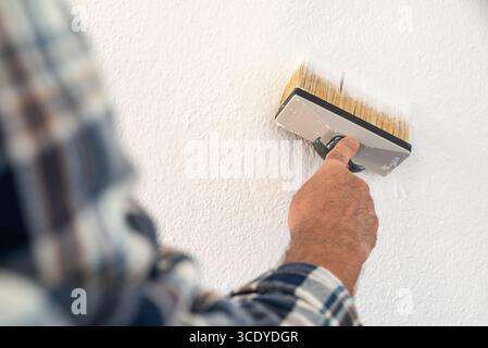 Close-up of a hand. A painter paints a masonry wall with white paint using using the paintbrush. Construction industry. Stock Photo