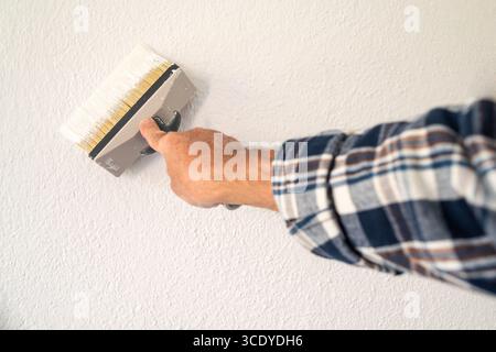 Close-up of a hand. A painter paints a masonry wall with white paint using using the paintbrush. Construction industry. Stock Photo