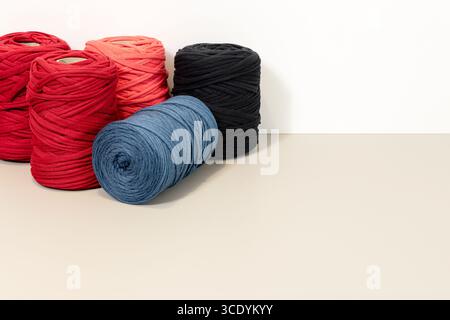 Background of a group of Spools of recycled t-shirt yarn arranged on a beige table against a white wall. Copy space Stock Photo