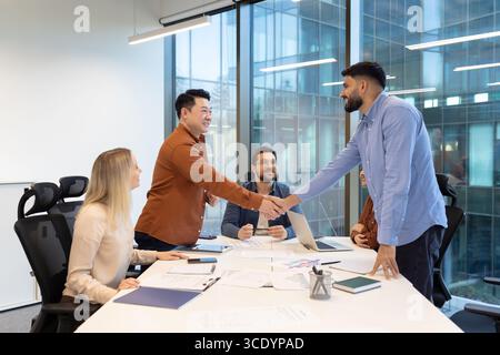 A group of professionals engaged in a collaborative meeting, discussing ideas while fostering teamwork in a modern office setting. Two colleagues are shaking hands, symbolizing professional agreement Stock Photo