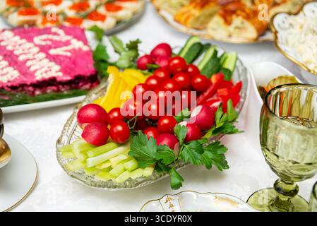 A colorful arrangement of fresh vegetables including radishes, cucumbers, tomatoes, and peppers on a glass platter, perfect for festive gatherings or Stock Photo