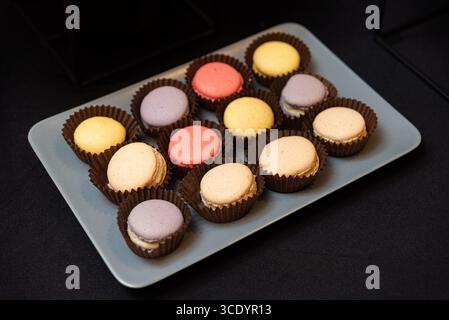 A variety of colorful macarons arranged on a plate. the pastel treats are set against a dark background, showcasing their vibrant hues and delicate te Stock Photo