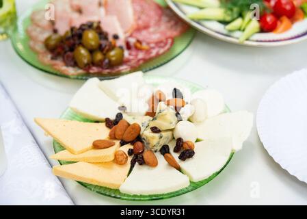 An appetizing cheese platter featuring a variety of cheeses, nuts, and olives, perfect for gatherings. plates of fresh vegetables and cold cuts comple Stock Photo