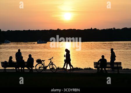 Berlin, Germany. 14th Aug, 2025. People walk along the shore of Lake Tegler See at sunset. Credit: Sebastian Gollnow/dpa/Alamy Live News Stock Photo