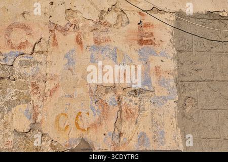 Close-up of a heavily weathered and textured concrete wall, with multiple layers of peeling paint revealing faded, illegible text, Sanremo, Italy Stock Photo
