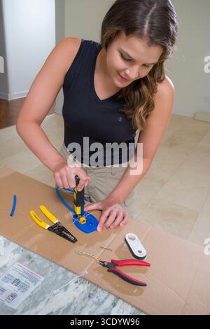 Young woman using a punch down tool to terminate blue Cat-6A ethernet cable to a Keystone module, USA Stock Photo