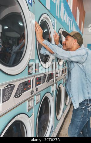 Man using washing machines in public laundromat for laundry routine Stock Photo