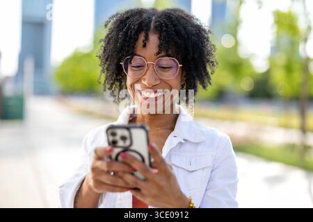 Portrait of a smiling young woman using mobile phone in the city Stock Photo
