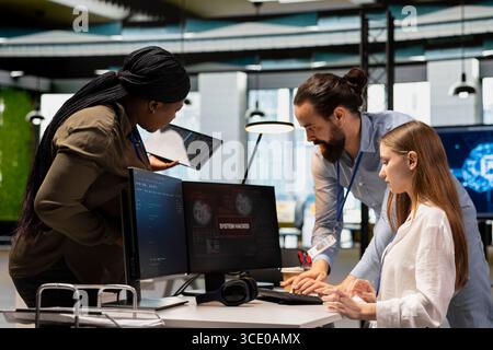 Young engineer in office requests help from IT experts detecting and blocking hacker intrusion. Female programmer assisted by staff members coordinating incident response for network attack Stock Photo