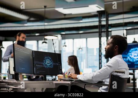 IT specialist in wheelchair developing software applications using AI automation. Programmer with paraplegia in inclusive office debugging applications with artificial intelligence Stock Photo