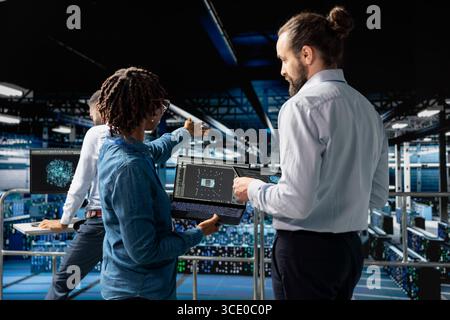 Server hub colleagues managing work by reviewing neural network code and LLM visualization for datasets. Technicians collaborating on AI system performance, industrial platform workstation. Stock Photo