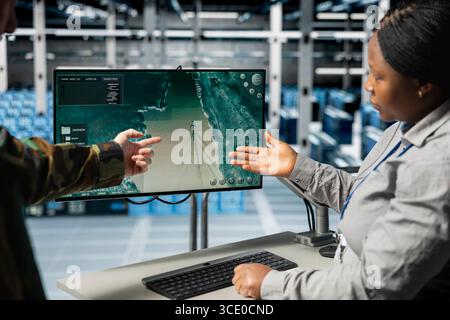 Team of military engineers in data center tracking satellite coordinates using monitor interface. Teamworking server room coworkers analyzing reconnaissance data through satellite imaging systems Stock Photo