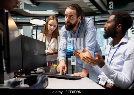 Team of programmers resolving critical error alert on screen in tech startup office, troubleshooting system warnings. IT staff members brainstorming fixes for office equipment failure Stock Photo