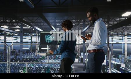 Engineers working together on data center industrial platform, completing software updates. Server hub colleagues doing brainstorming, finetuning server rig configurations, Stock Photo