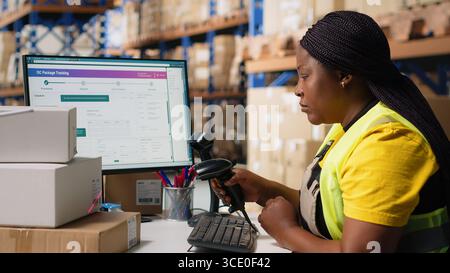 Black employee scanning awb tags after packaging operations in a distribution center, using a scanner to register barcode shipping labels for future order tracking. Storage room. Camera B. Stock Photo