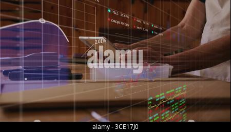 Reviewing financial charts while holding tablet above plastic tray at wooden kitchen counter Stock Photo