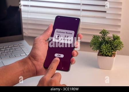 Man give a good rating to customer review on smartphone. Positive feedback or customer review satisfaction feedback concept. Stock Photo