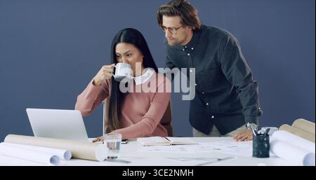 Coffee, laptop and architects with blueprints in office for city planning, email or meeting. Computer, cappuccino and construction designers in Stock Photo
