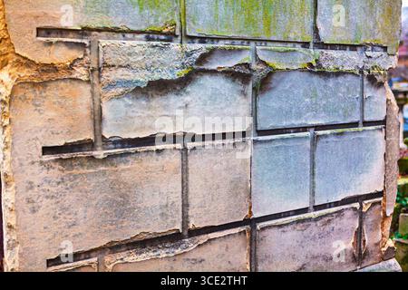 Weathered and crumbling stone wall with rectangular blocks. Surface is deteriorating, with patches of green moss and exposed, rough edges. Wall part Stock Photo