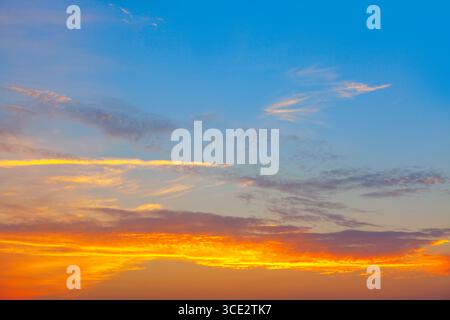 Sunset sky fades from deep blue to fiery orange near the horizon. Thin clouds streak across, adding motion and contrast to the glowing gradient Stock Photo