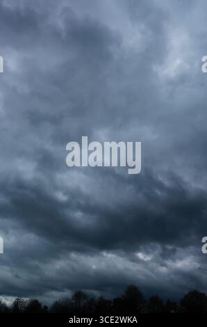 Dramatic storm clouds gathering over a dark landscape, ominous weather scene Stock Photo